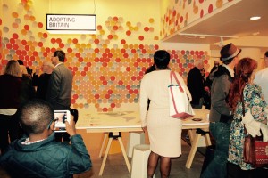 Visitors look at paper discs on wall, which visitors have written their migration/non-migration stories on before hanging up. A young boy in the foreground captures the scene on a tablet camera.