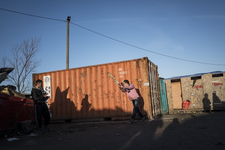 Calais, France. 08/01/16. A group of Afghan men play cricket against a shipping container in an area of the Calais 'Jungle' refugee camp known as 'Afghan Square'.