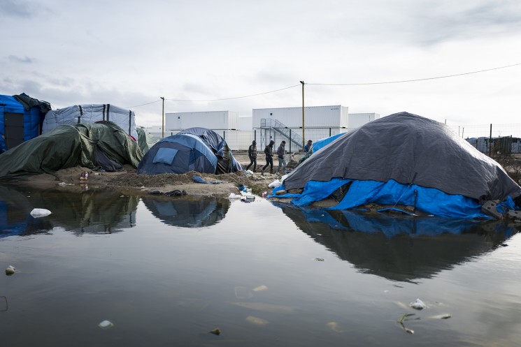 Calais, France. 09/01/16. A group of refugees walk past the new section of the Calais 'Jungle' refugee camp. 1500 places have been made available in converted shipping containers, but a place is conditional on registering with a handpring which many camp residents worry may jeopardise their asylum status in other countries.