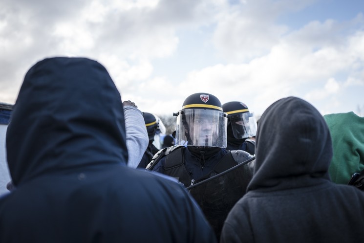 Calais, France. 07/03/16. A French CRS riot policeman remonstrates with Eritrean refugees who are to lose their shelters today. French authorities are evicting and demolishing the southern half of the Calais 'Jungle' camp, which charities estimate to contain 3,500 people.