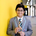 Pupil in uniform holds wooden giraffe in corridor of school.